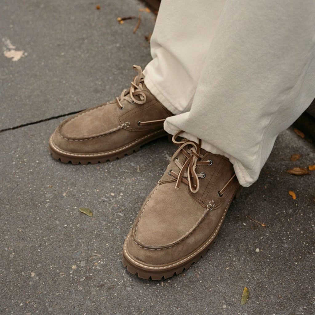 Men's Larkspur Lug Boat Shoe in Cement suede, worn with cream pants on a gray sidewalk