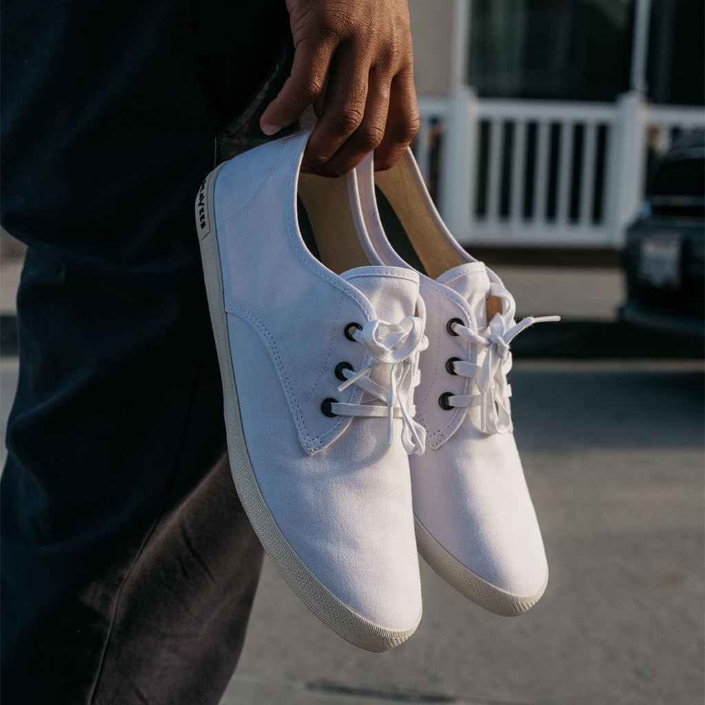 Men's Sixty Six Sneaker in White canvas, pair held in hand by a person standing on a street