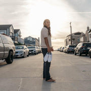Men's Sixty Six Sneaker in White canvas, pair held in hand by a barefoot person standing in a street at sunset