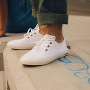 Men's Sixty Six Sneaker in White canvas, close-up with laces, worn with cuffed olive pants on a wooden step