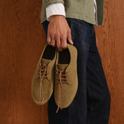 Men's Sun-tans Buck in Dusty Olive suede, held up in one hand in front of dark jeans