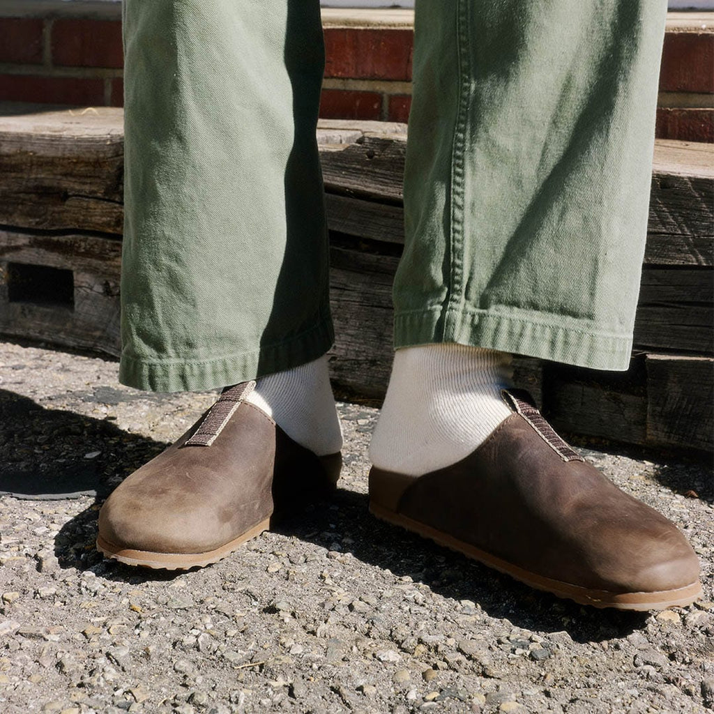 Men's Tiburon Trekker sandal in Bark leather, worn with olive pants and white socks on gravel