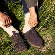 Men's Tiburon Trekker sandal in Espresso suede, worn with cream socks, being pulled on in tall grass
