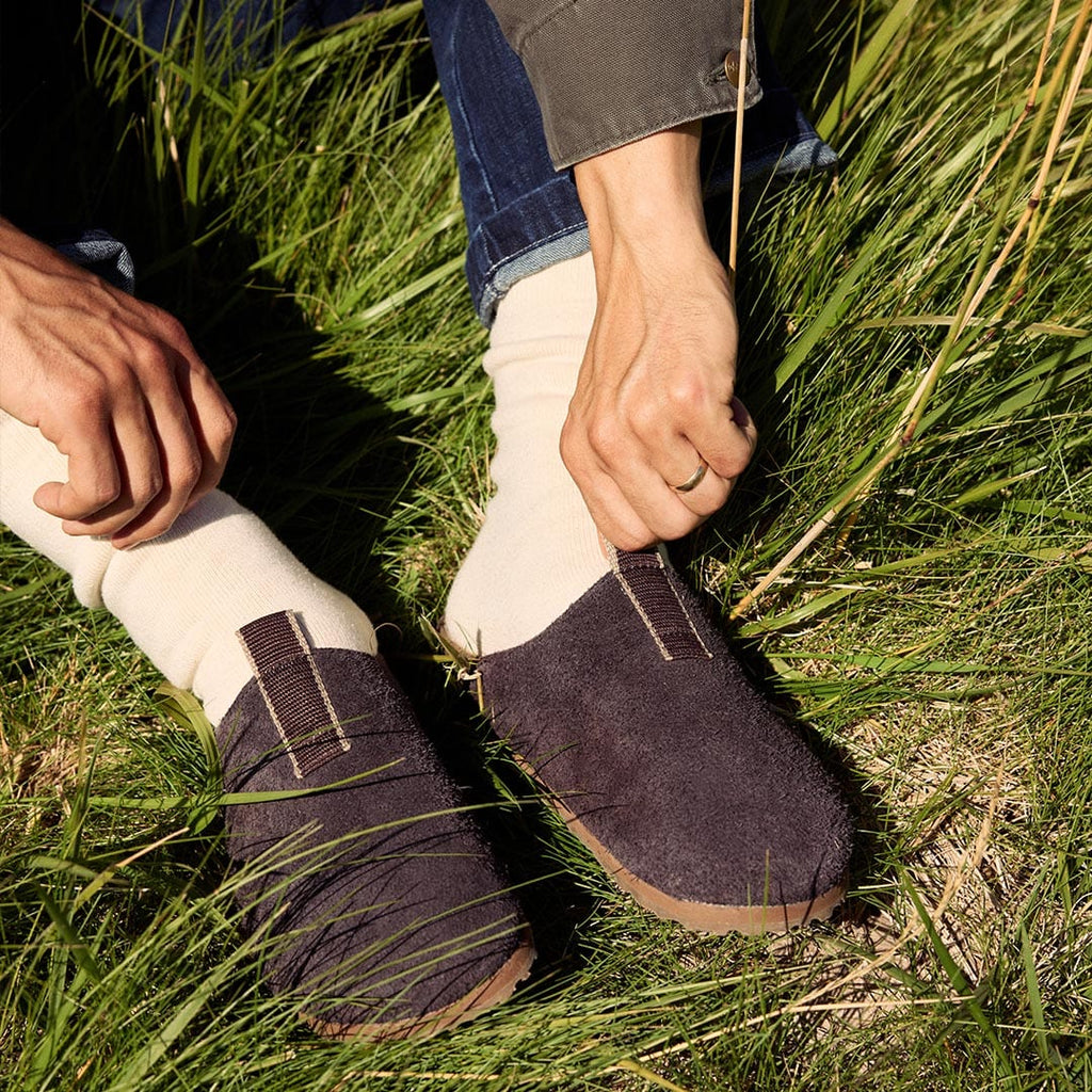 Men's Tiburon Trekker sandal in Espresso suede, worn with cream socks, being pulled on in tall grass