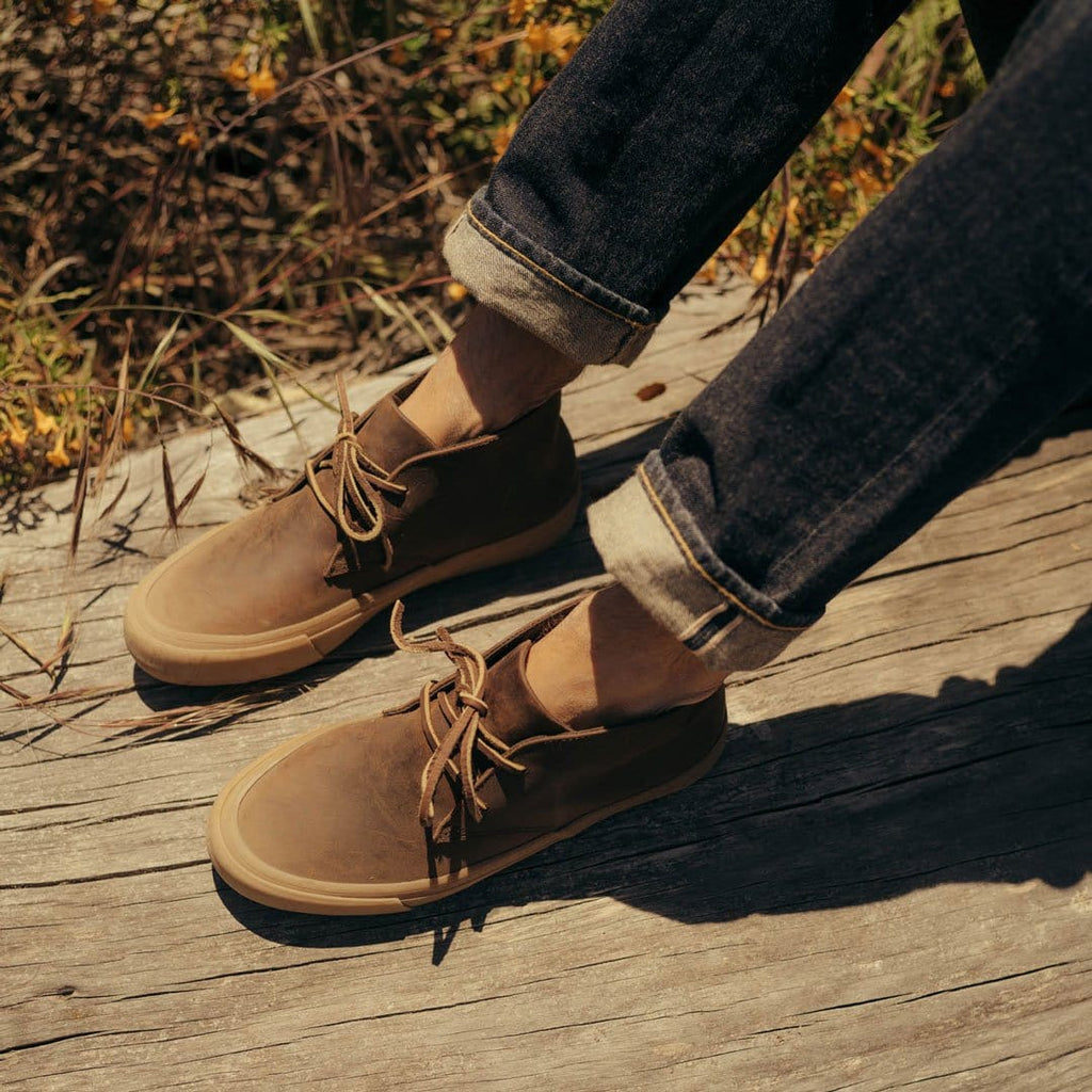 Men's Maslon Desert Boot in Kona leather, close-up worn with cuffed jeans on a wooden deck