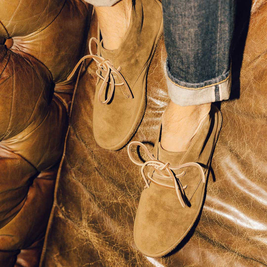 Men's Sun-tans Chukka in Desert Palm suede, close-up worn with cuffed jeans on a leather sofa