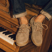 Men's Sun-tans Buck in Fossil suede, close-up worn with cuffed jeans, feet resting on a piano