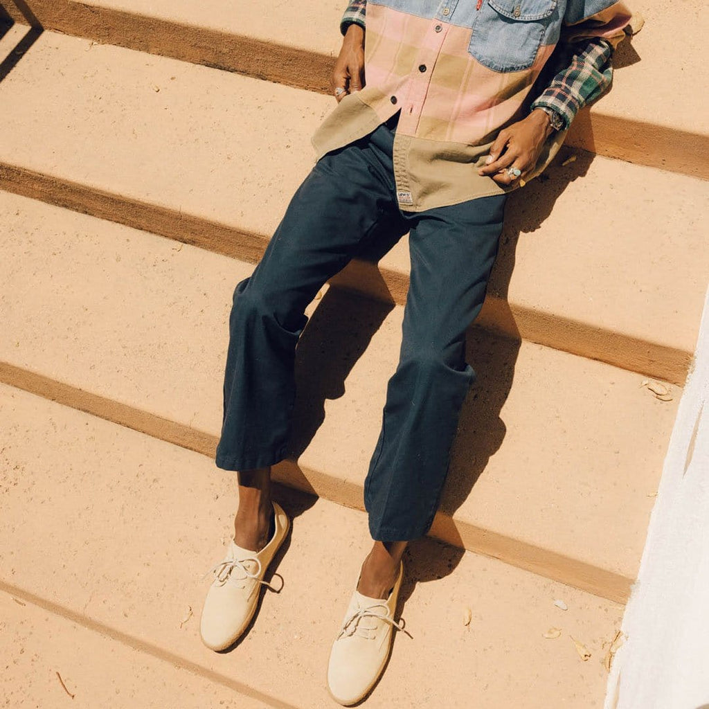 Men's Sun-tans Buck in Sandstone suede, worn with navy pants by a person seated on sandy-colored steps