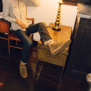 Men's Sun-tans Chukka in Desert Palm suede, worn with jeans by a person seated beside a table lamp