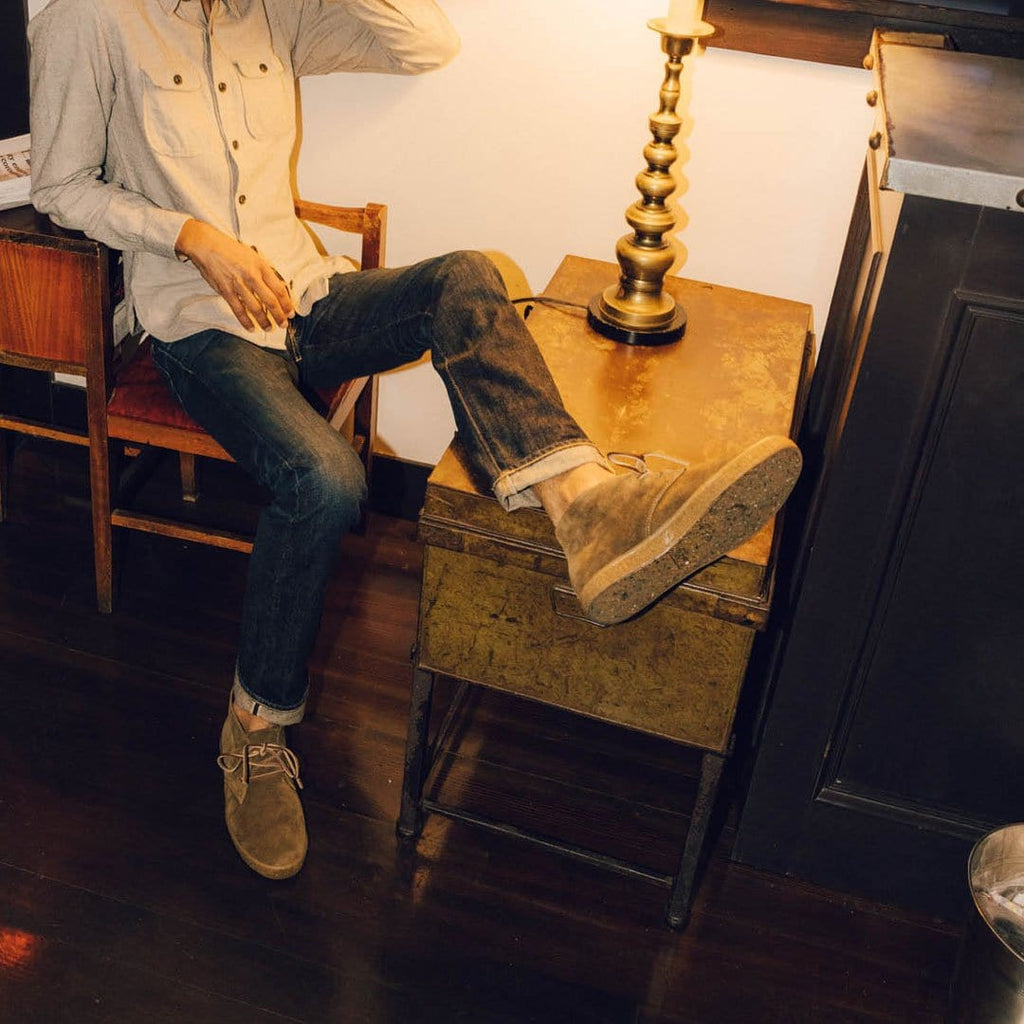 Men's Sun-tans Chukka in Desert Palm suede, worn with jeans by a person seated beside a table lamp