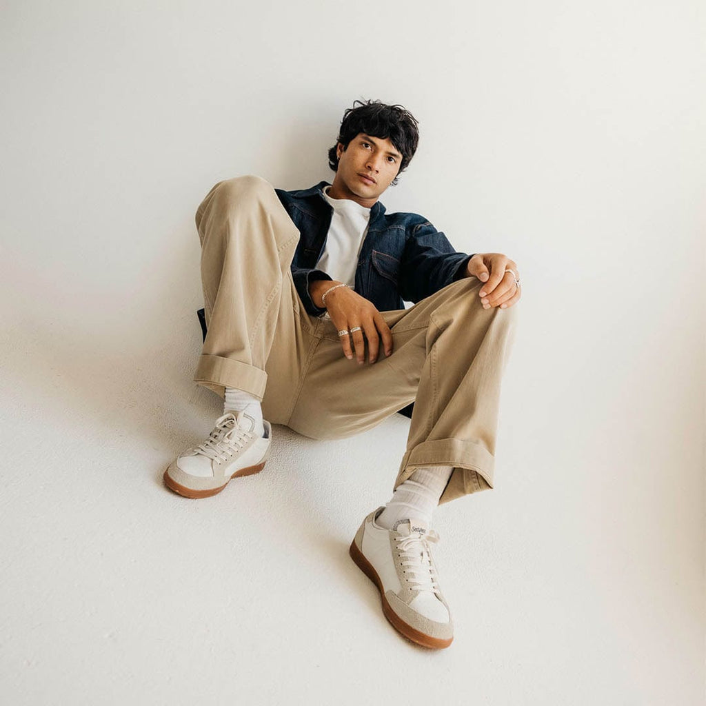 Men's Clipper Sneaker in White leather and suede, worn by a person seated on a studio floor in khaki pants