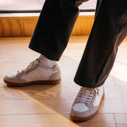 Men's Clipper Sneaker in White leather and suede, worn with black pants on a light wood floor