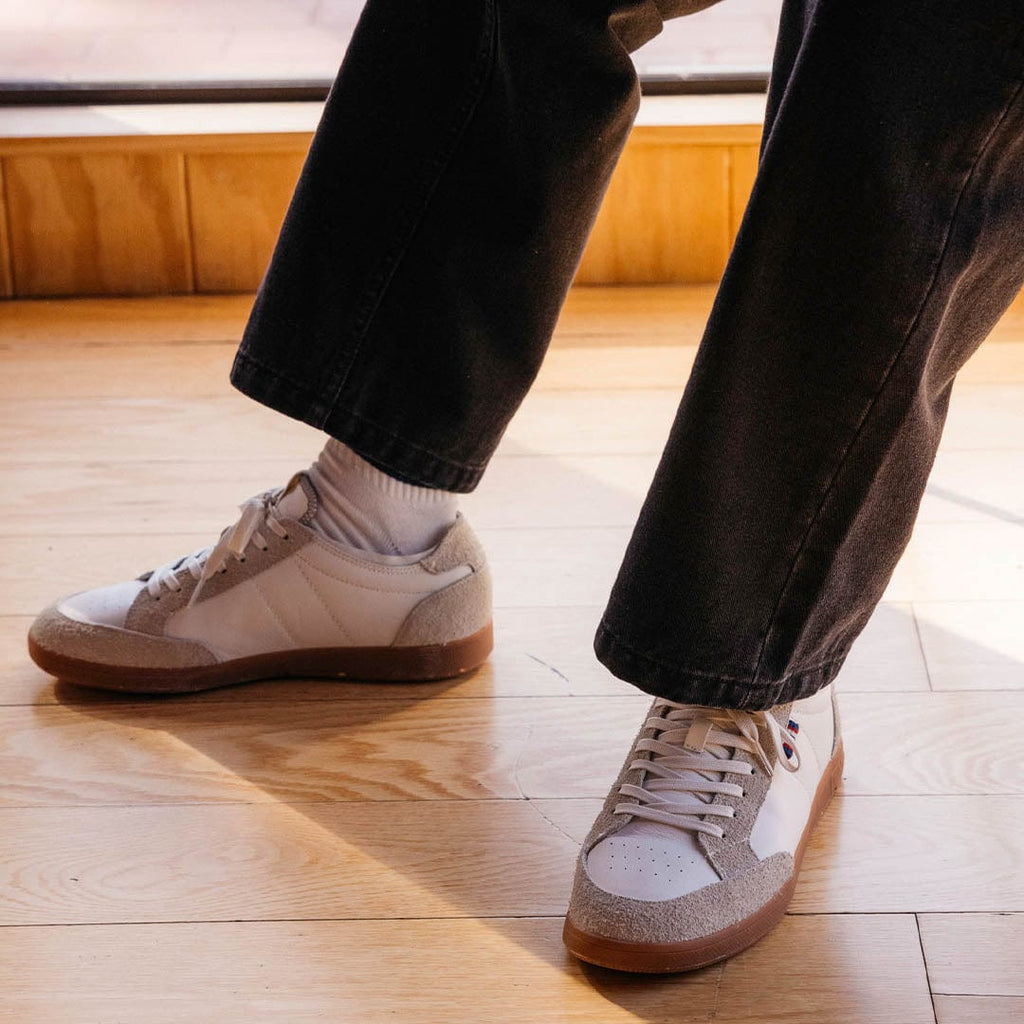 Men's Clipper Sneaker in White leather and suede, worn with black pants on a light wood floor
