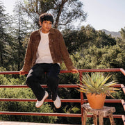 Men's Clipper Sneaker in White leather and suede, worn by a person seated on a railing above a hillside