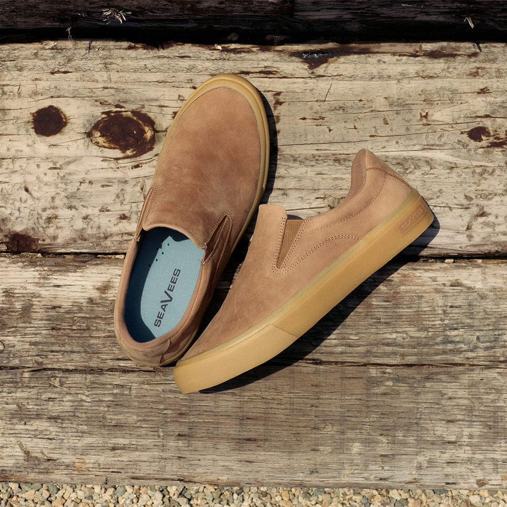 Men's Hawthorne Slip On in Sandstorm leather, pair resting on a weathered wooden beam