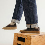 Men's Hawthorne Slip On in Kona leather, worn with cuffed jeans, feet resting on a wooden crate