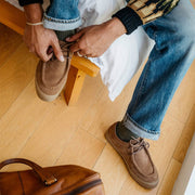 Men's Hayward Loafer in Tobacco suede, worn by a person lacing the shoe, seated on a bench