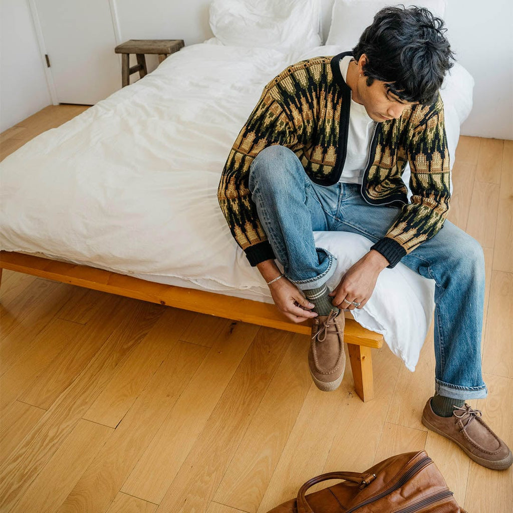 Men's Hayward Loafer in Tobacco suede, worn by a person seated on a bed tying the laces