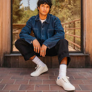 Men's Legend Sneaker in Bleach canvas, worn with white socks by a person seated in a window frame