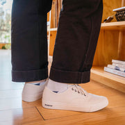 Men's Legend Sneaker in Bleach canvas, close-up worn with cuffed pants in front of a bookshelf