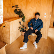 Men's Legend Sneaker in Bleach canvas, worn with white socks by a person seated in a plywood room