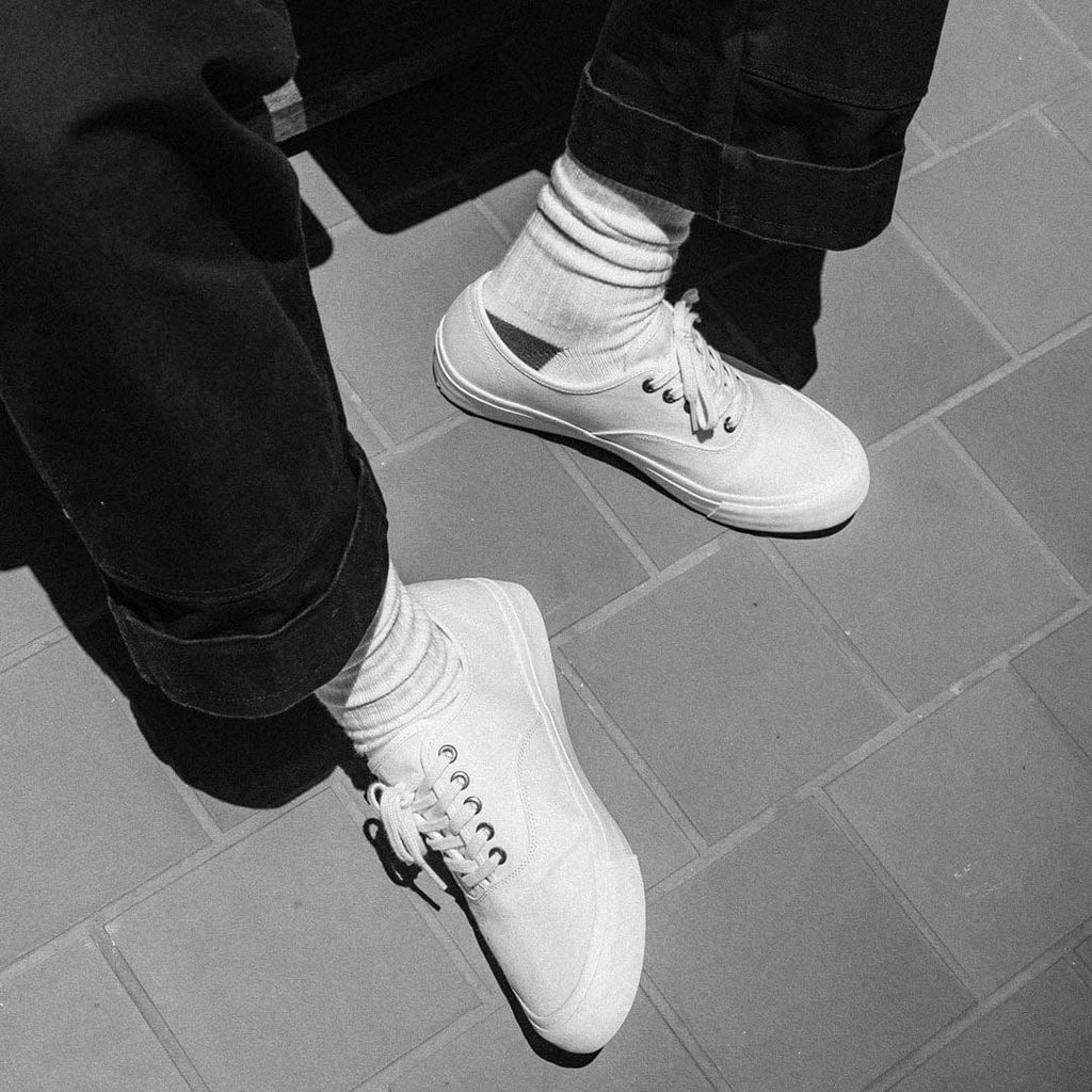 Men's Legend Sneaker in Bleach canvas, close-up of laces and white socks on a gray tile floor