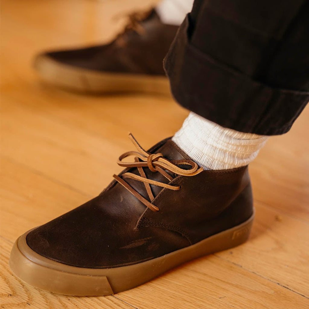 Men's Maslon Desert Boot in Kona leather, close-up of laces, worn with white socks on a wood floor