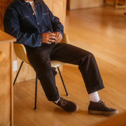 Men's Maslon Desert Boot in Kona leather, worn with white socks and cuffed pants by a person seated on a chair