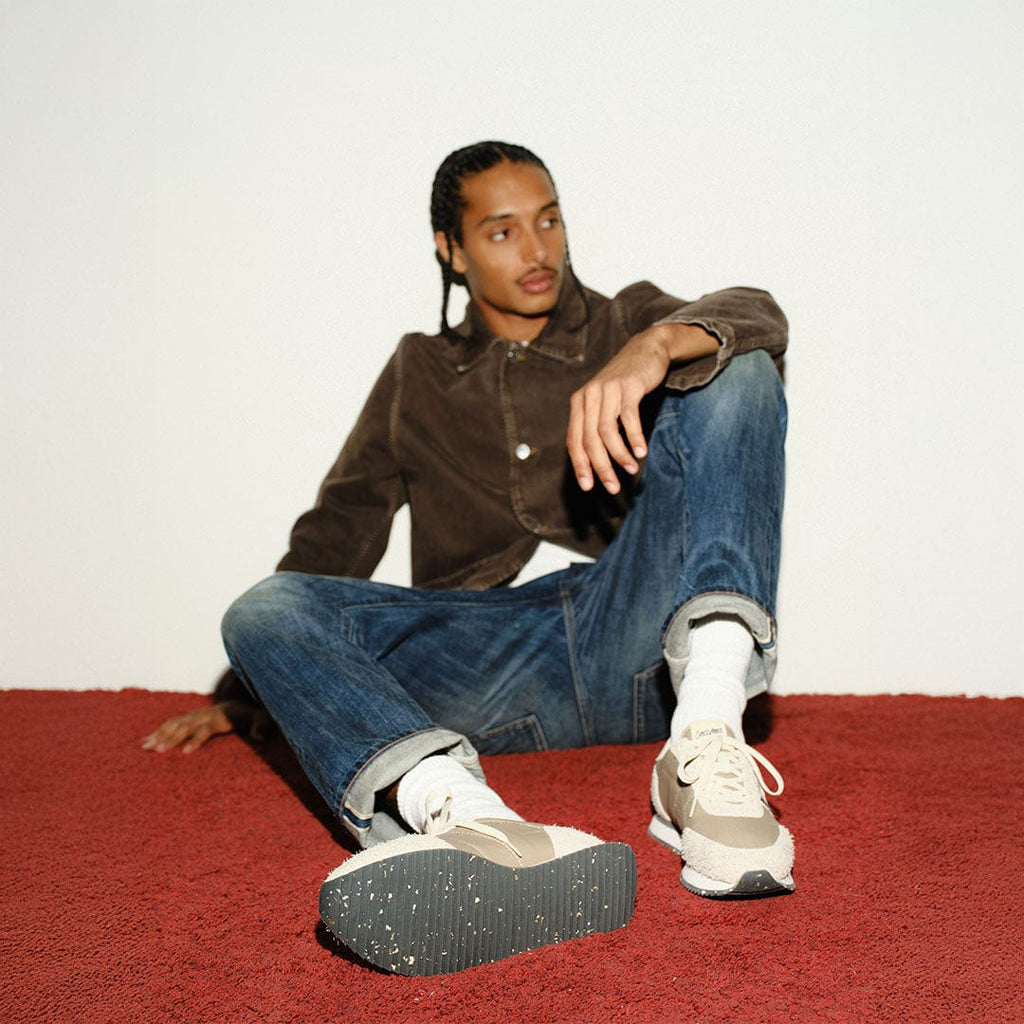 Men's Royal Runner sneaker in Latte nylon and suede, worn by a person seated on a red carpet in jeans