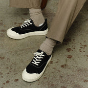 Men's Sato Oxford in Black canvas, worn with khaki pants and gray socks on a concrete floor