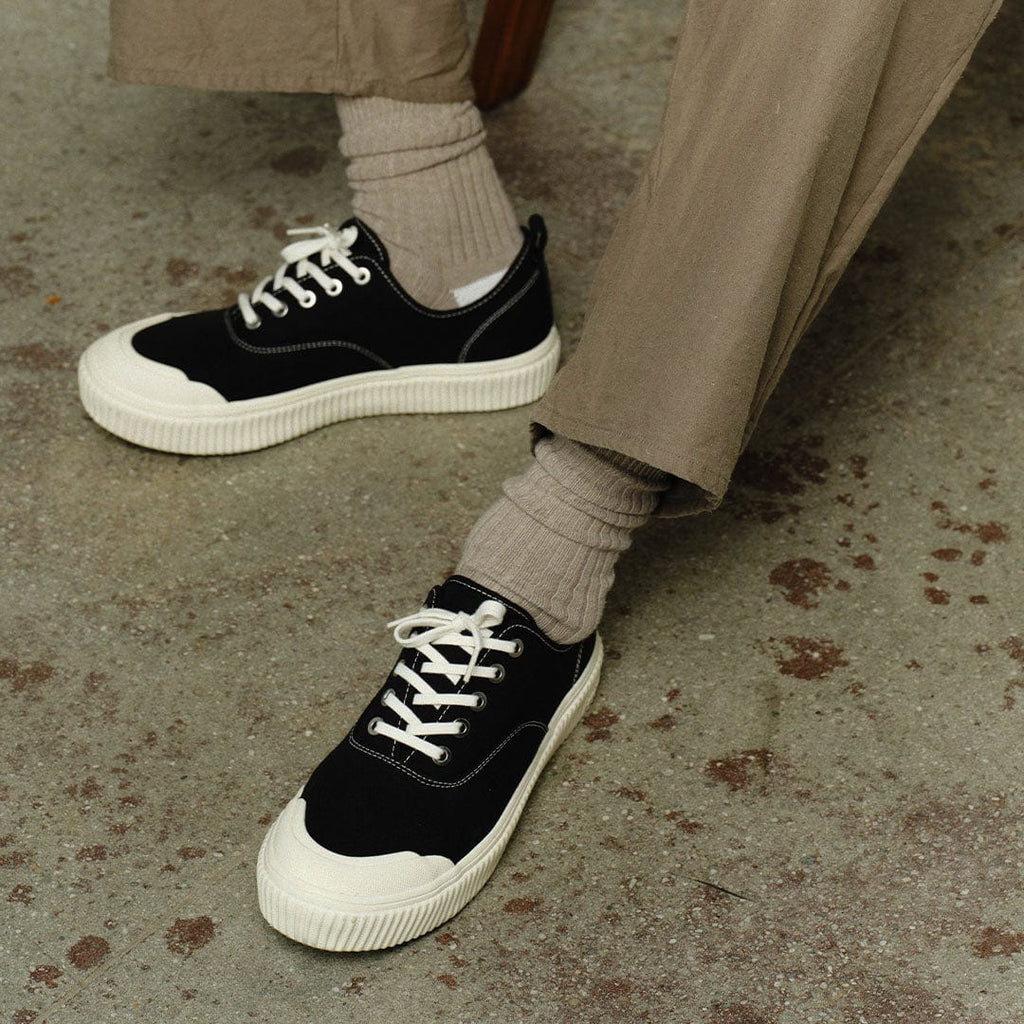 Men's Sato Oxford in Black canvas, worn with khaki pants and gray socks on a concrete floor