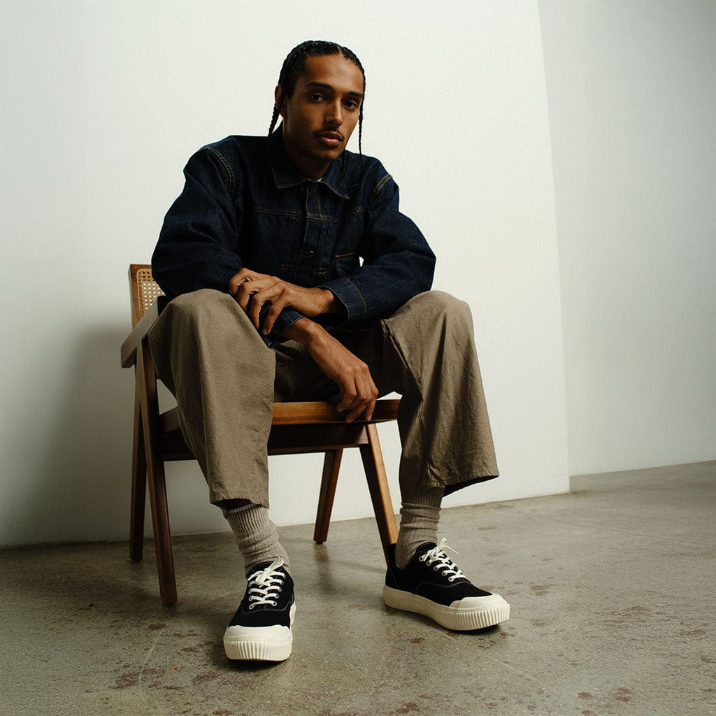 Men's Sato Oxford in Black canvas, worn by a person seated in a wooden chair in khaki pants