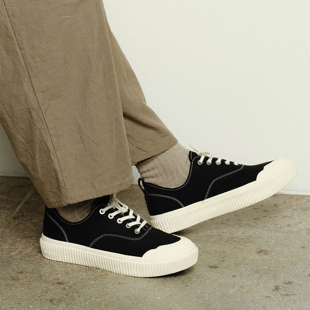 Men's Sato Oxford in Black canvas, worn with khaki pants on a concrete floor, close up