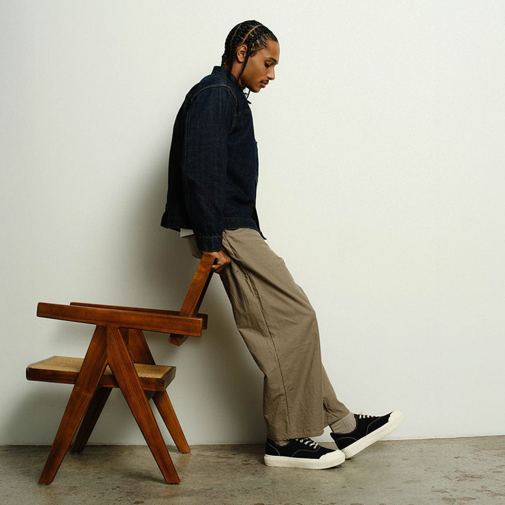 Men's Sato Oxford in Black canvas, worn by a person leaning on a wooden chair in a dark jacket