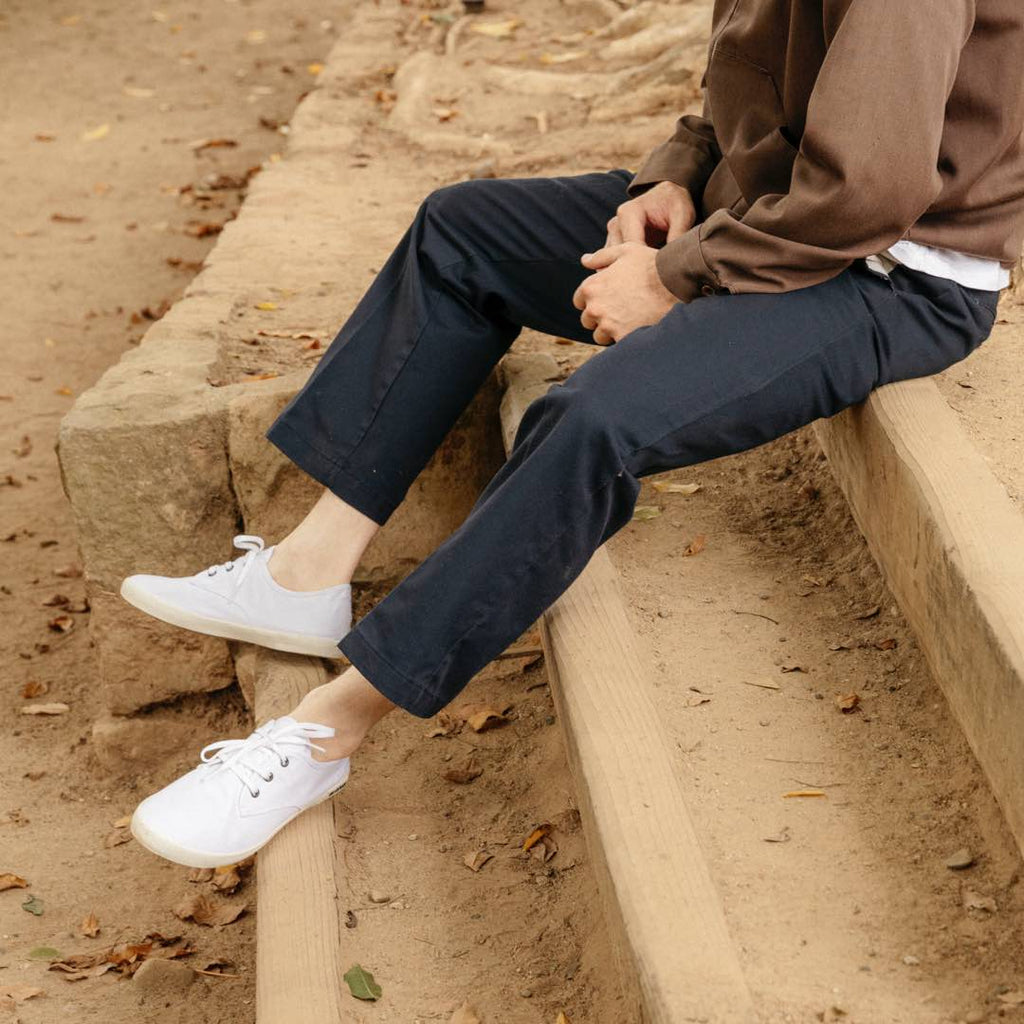 Men's Sixty Six Sneaker in White canvas, worn with dark jeans by a person seated on stone steps