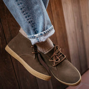 Men's Sun-tans Chukka in Desert Palm suede, close-up worn with cuffed jeans against a wood wall