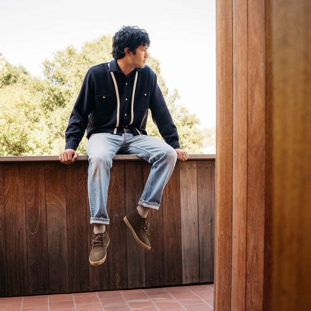 Men's Sun-tans Chukka in Desert Palm suede, worn with light jeans by a person seated on a wooden railing