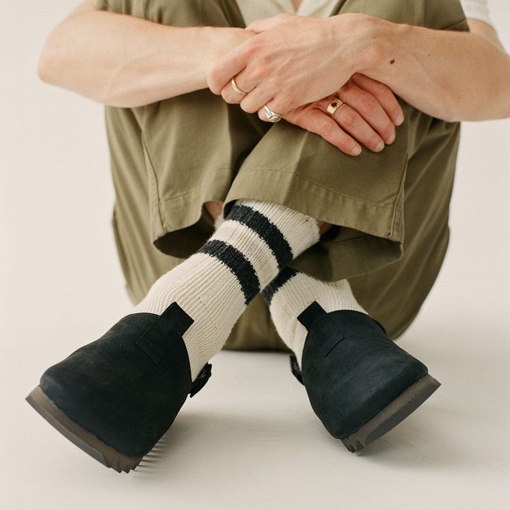 Men's Tahoe Trekker sandal in Black leather, worn with striped cream socks, seated on a studio floor