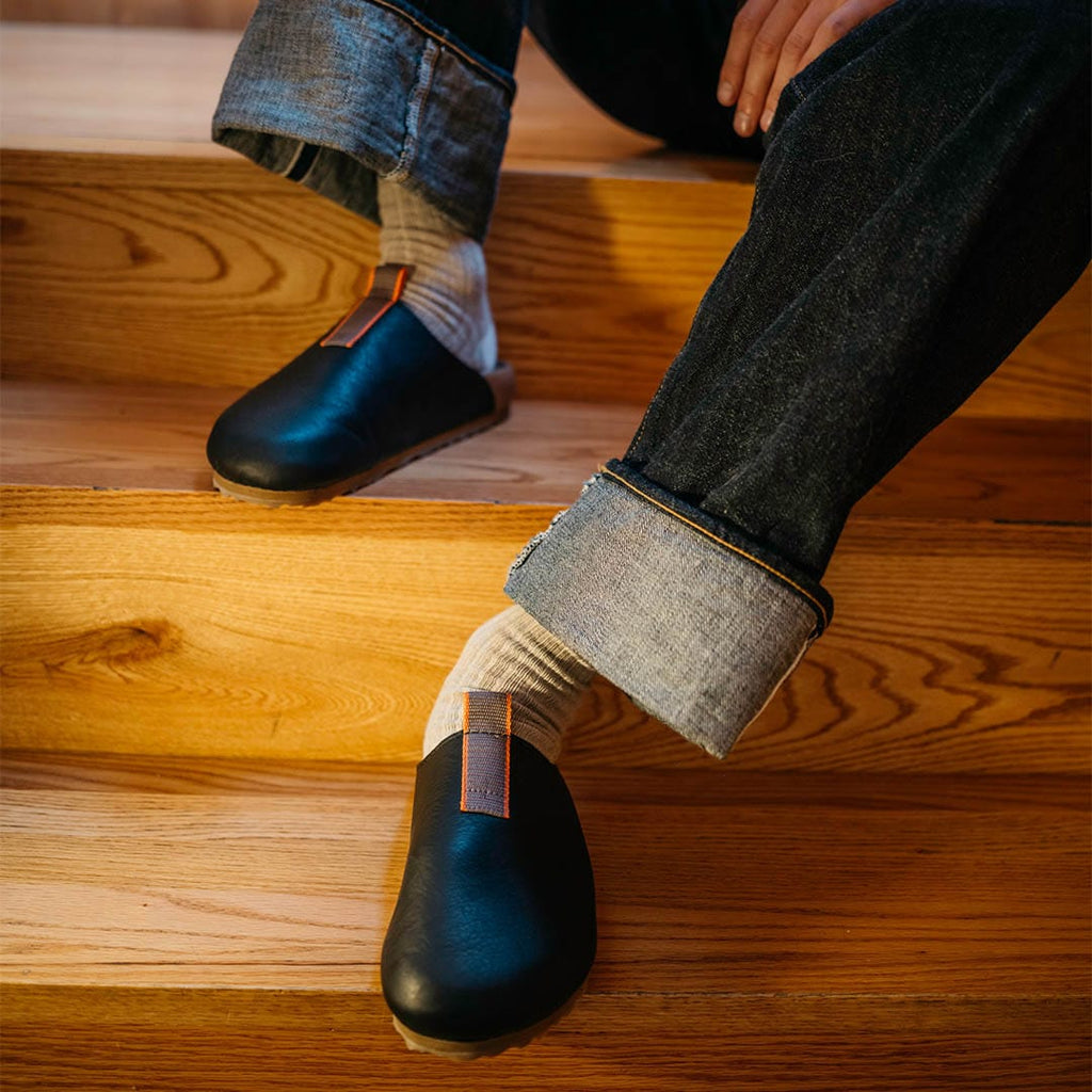 Men's Tiburon Trekker sandal in Black leather, worn with rolled jeans on wooden stairs