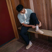 Men's Tiburon Trekker sandal in Maple suede, worn by a person seated on a wooden bench in a small cabin