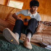 Men's Tiburon Trekker sandal in Maple suede, worn by a person seated on a sofa playing guitar