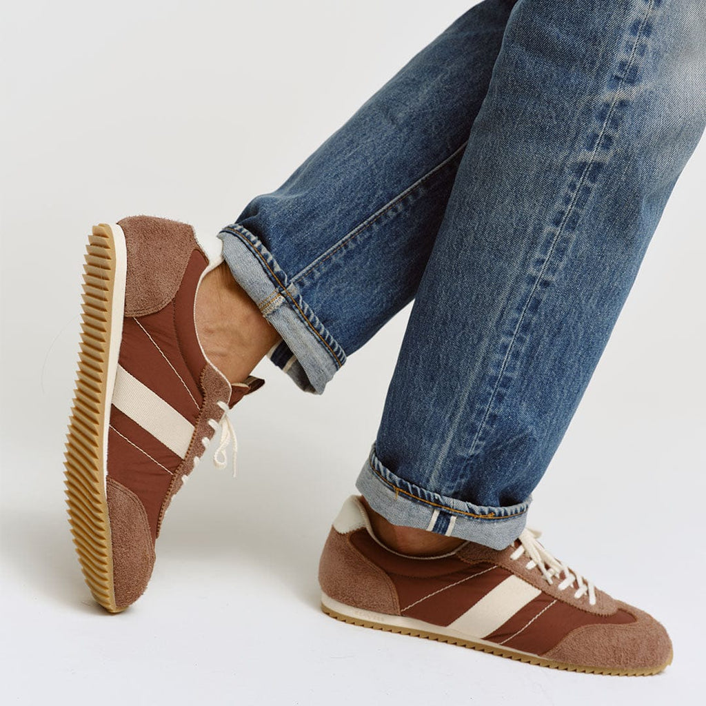 Men's Wilcox Low Profile Trainer sneaker in Cinnamon nylon and suede, worn with cuffed jeans, one foot raised showing the gum