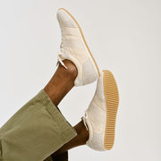 Men's Wilcox Low Profile Trainer sneaker in Cloud nylon and suede, worn with olive pants, one foot raised showing the gum
