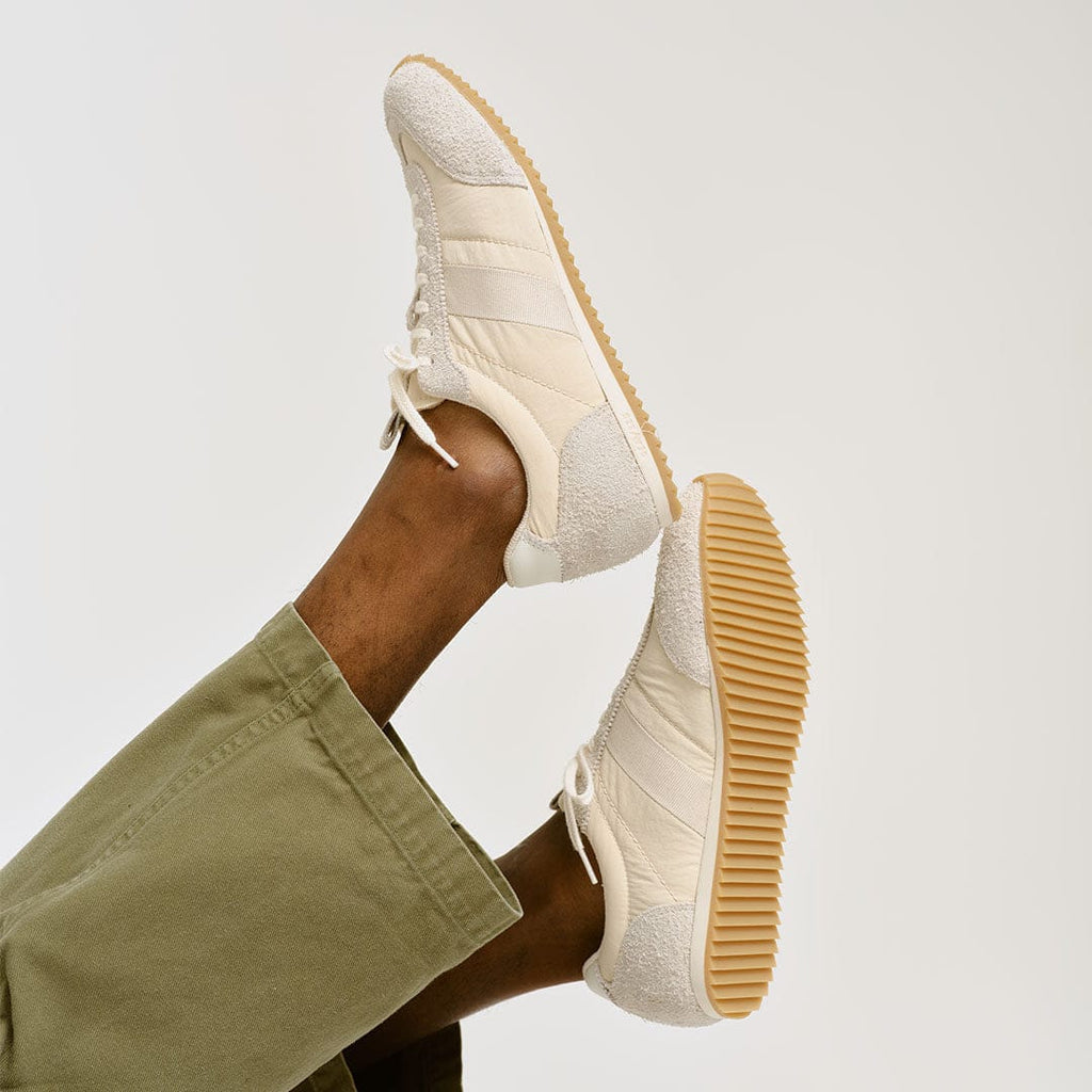 Men's Wilcox Low Profile Trainer sneaker in Cloud nylon and suede, worn with olive pants, one foot raised showing the gum