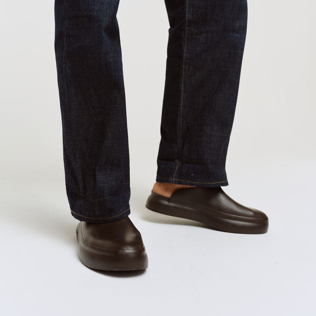 Men's Williams Mule in Dark Chocolate rubber, worn with dark jeans on a white background