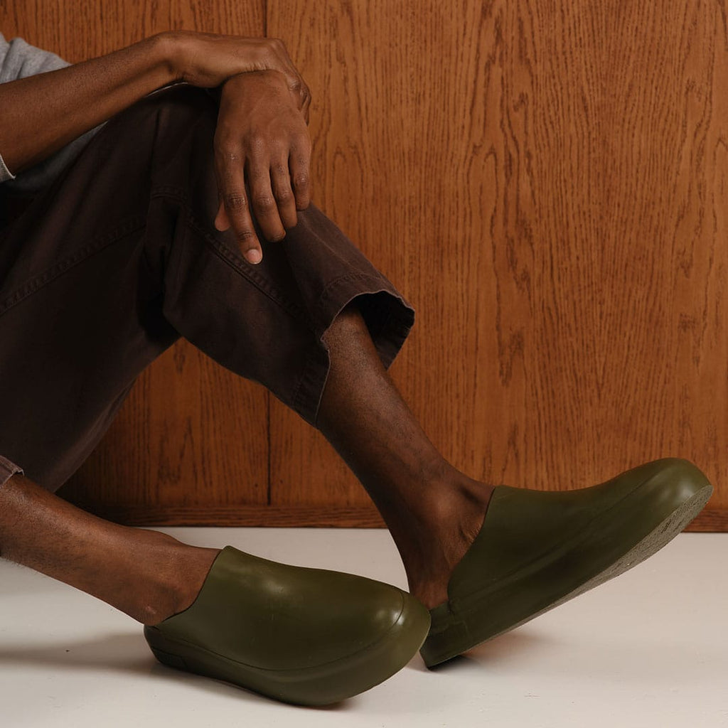 Men's Williams Mule in Utility Olive rubber, worn with brown pants, seated, close up