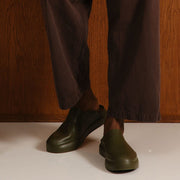 Men's Williams Mule in Utility Olive rubber, worn with dark pants against a wood wall