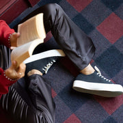Women's Monterey Sneaker in Black canvas, worn with black pants by a person reading on a plaid blanket