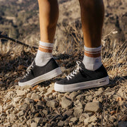 Women's Monterey Sneaker in Black canvas, close-up worn with striped socks on rocky ground