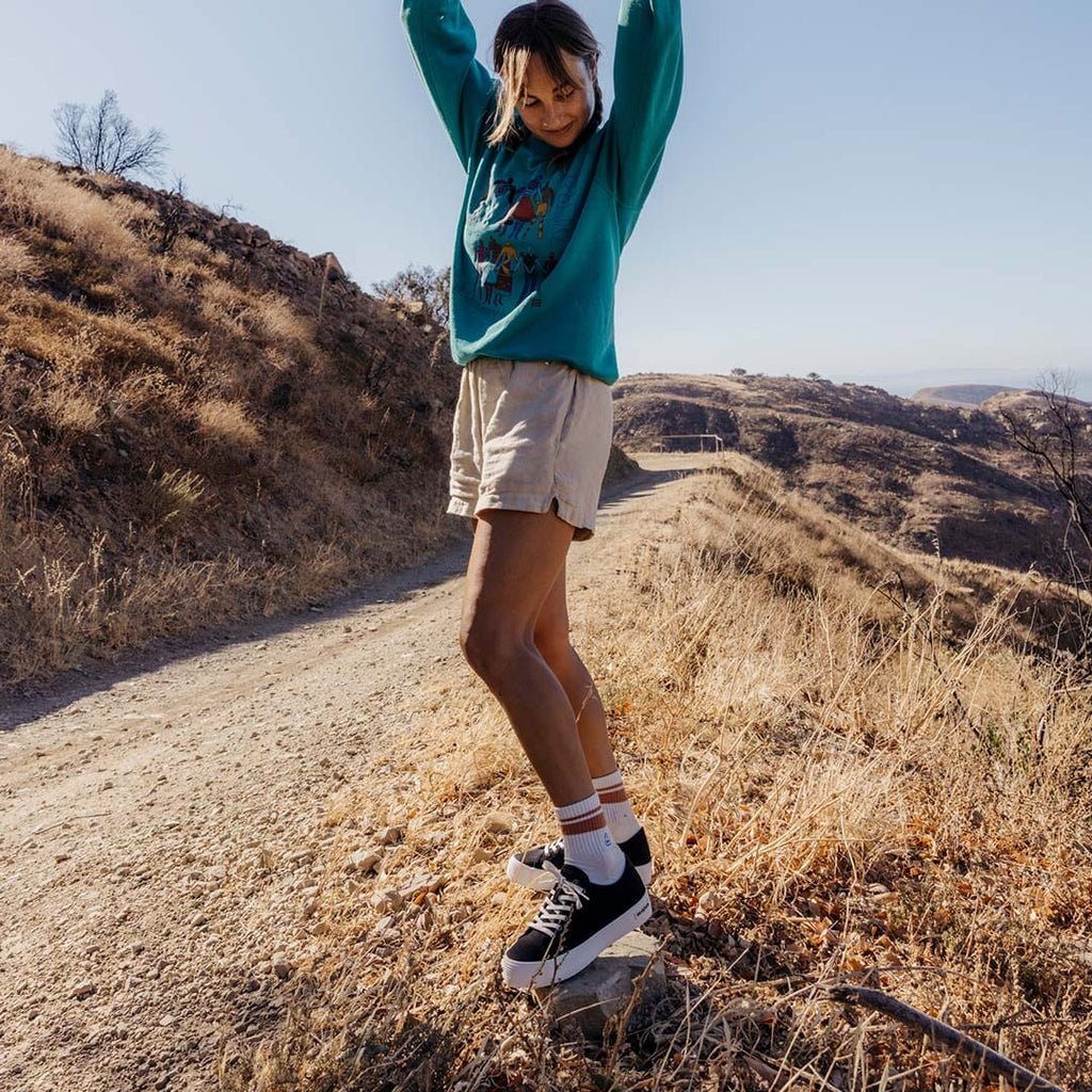 Women's Monterey Sneaker in Black canvas, worn with shorts by a person hiking a dirt trail